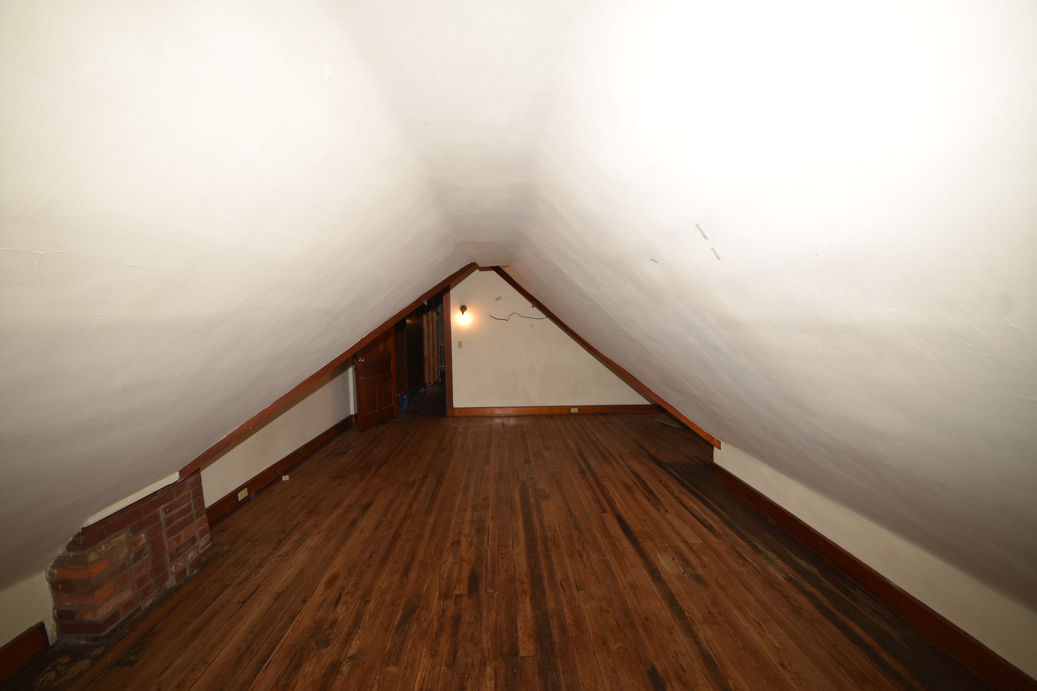 Attic room with sloped ceiling, wood floor, and exposed brick