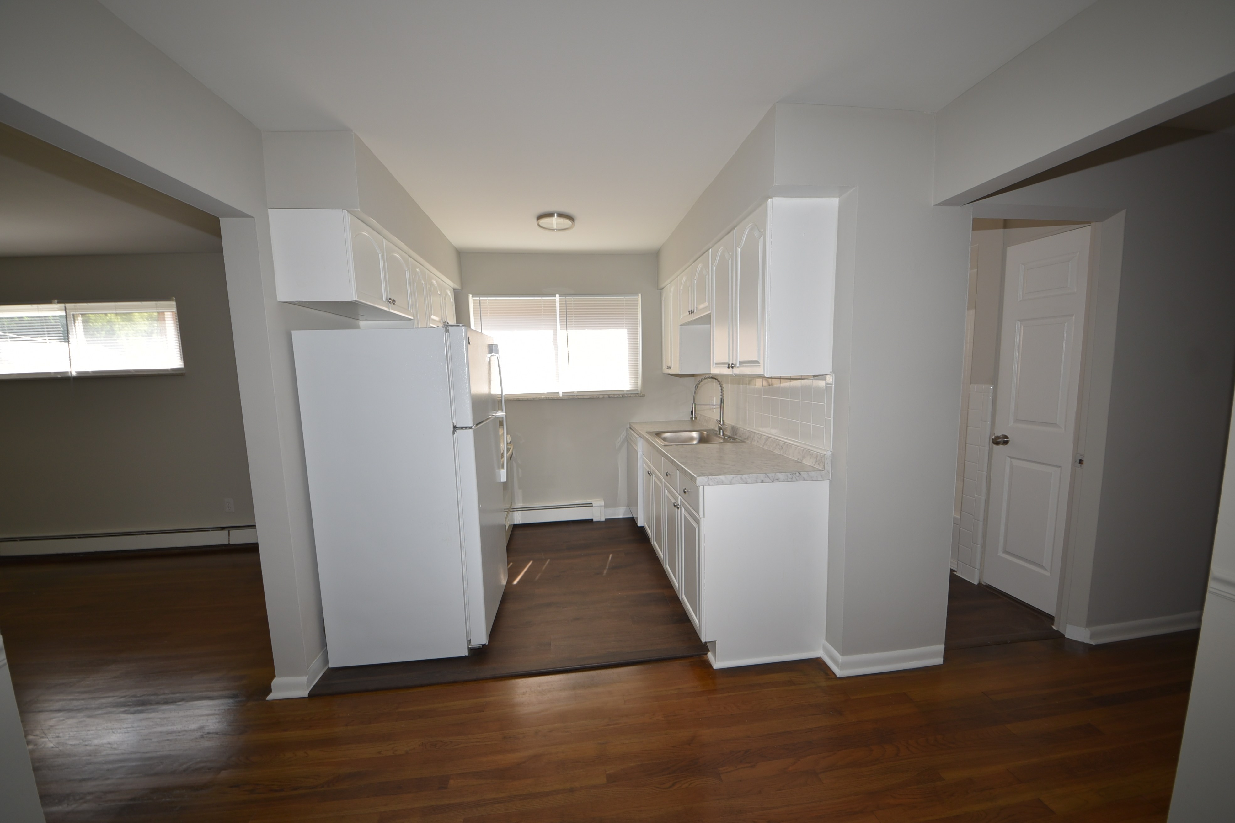 Galley kitchen with white cabinets, sink, and window