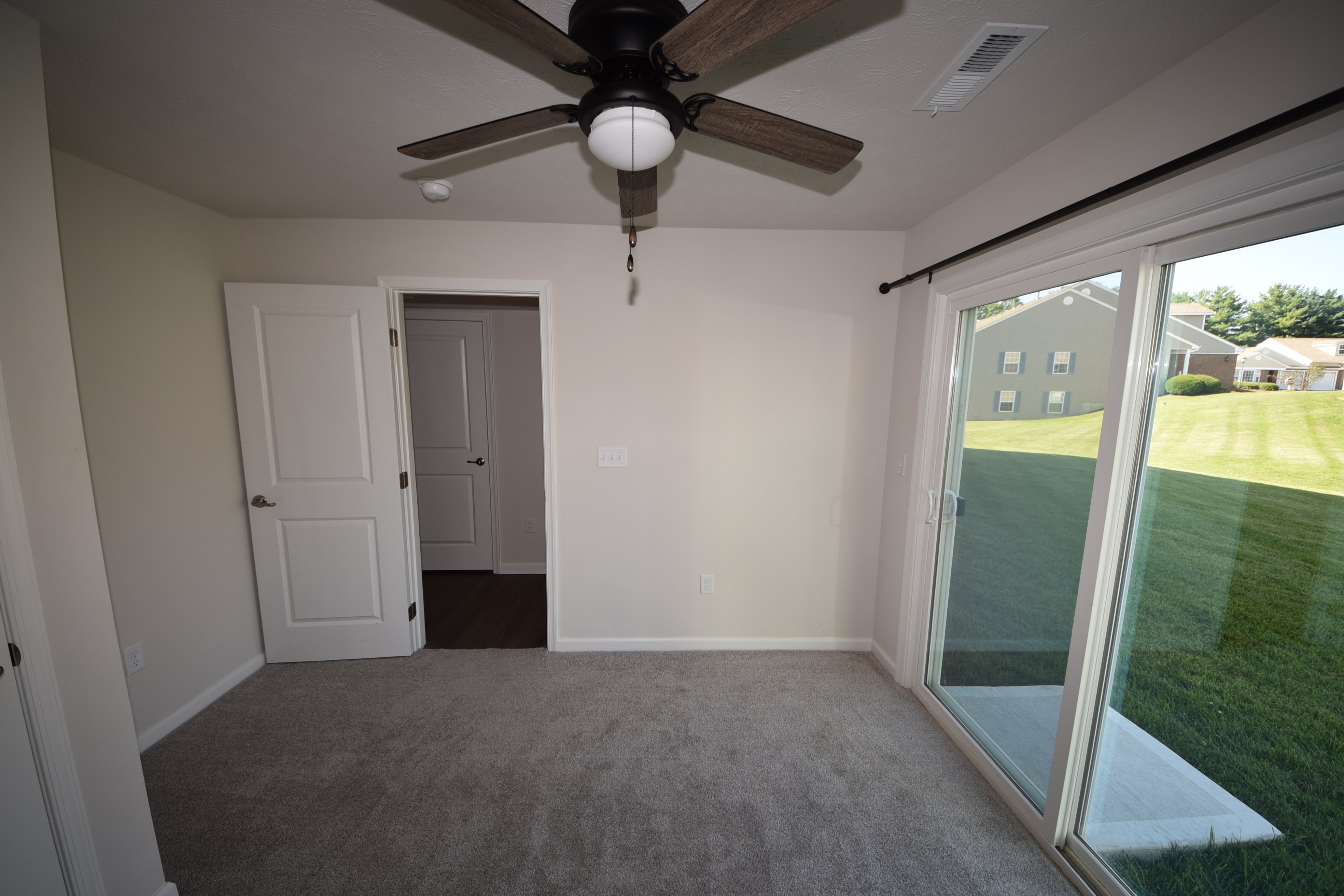 Carpeted room with sliding glass door and ceiling fan