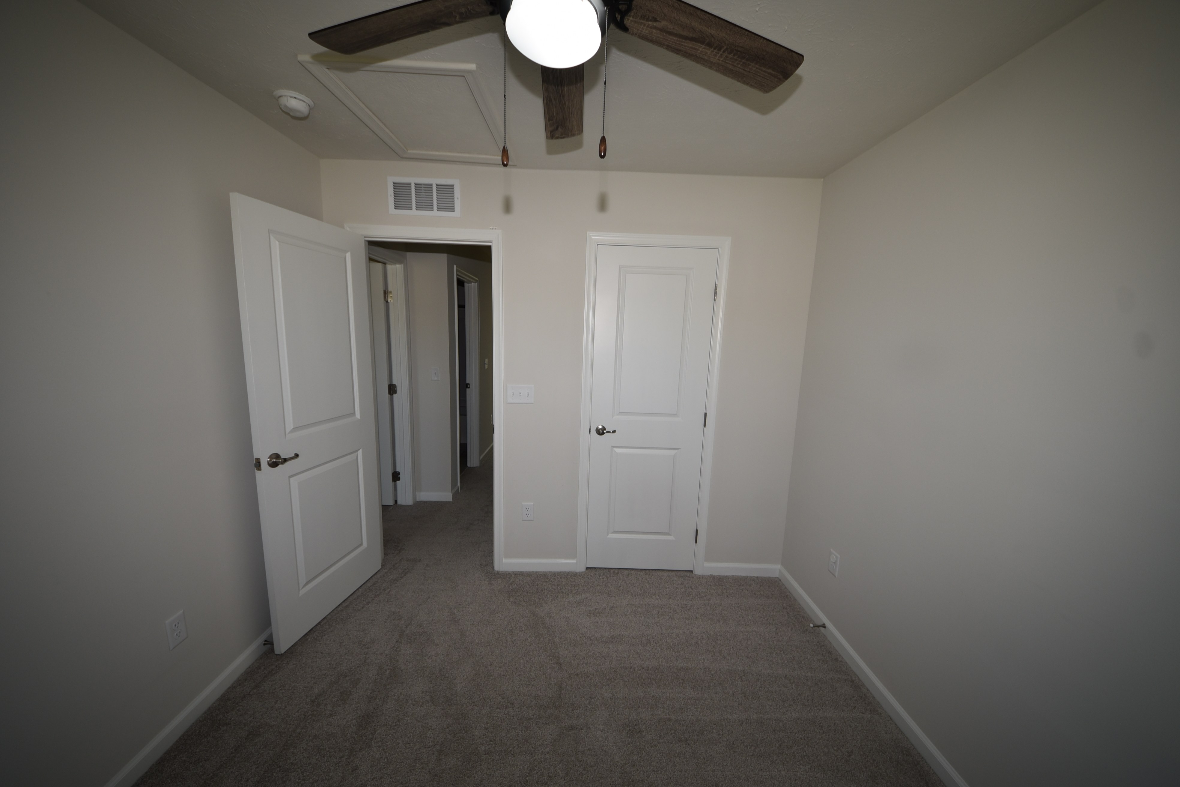 Carpeted bedroom with open doorway and ceiling fan