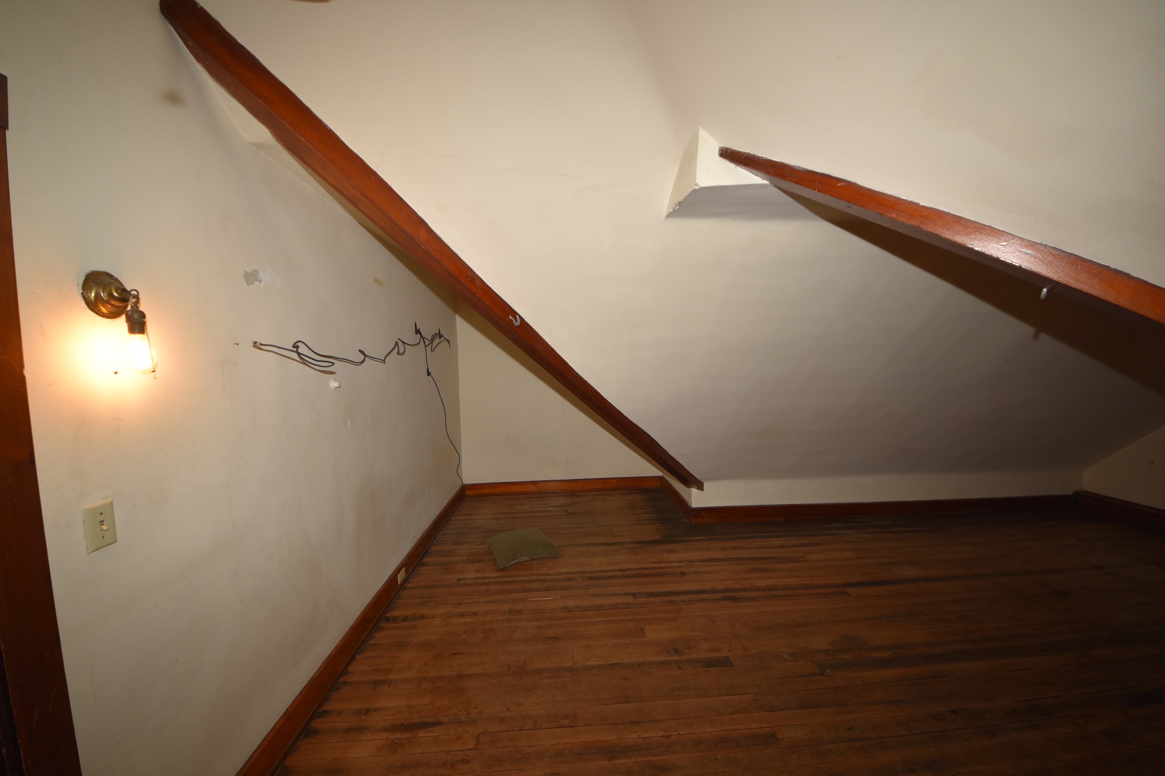 Attic room with angled ceiling, wood floor, and wall-mounted light