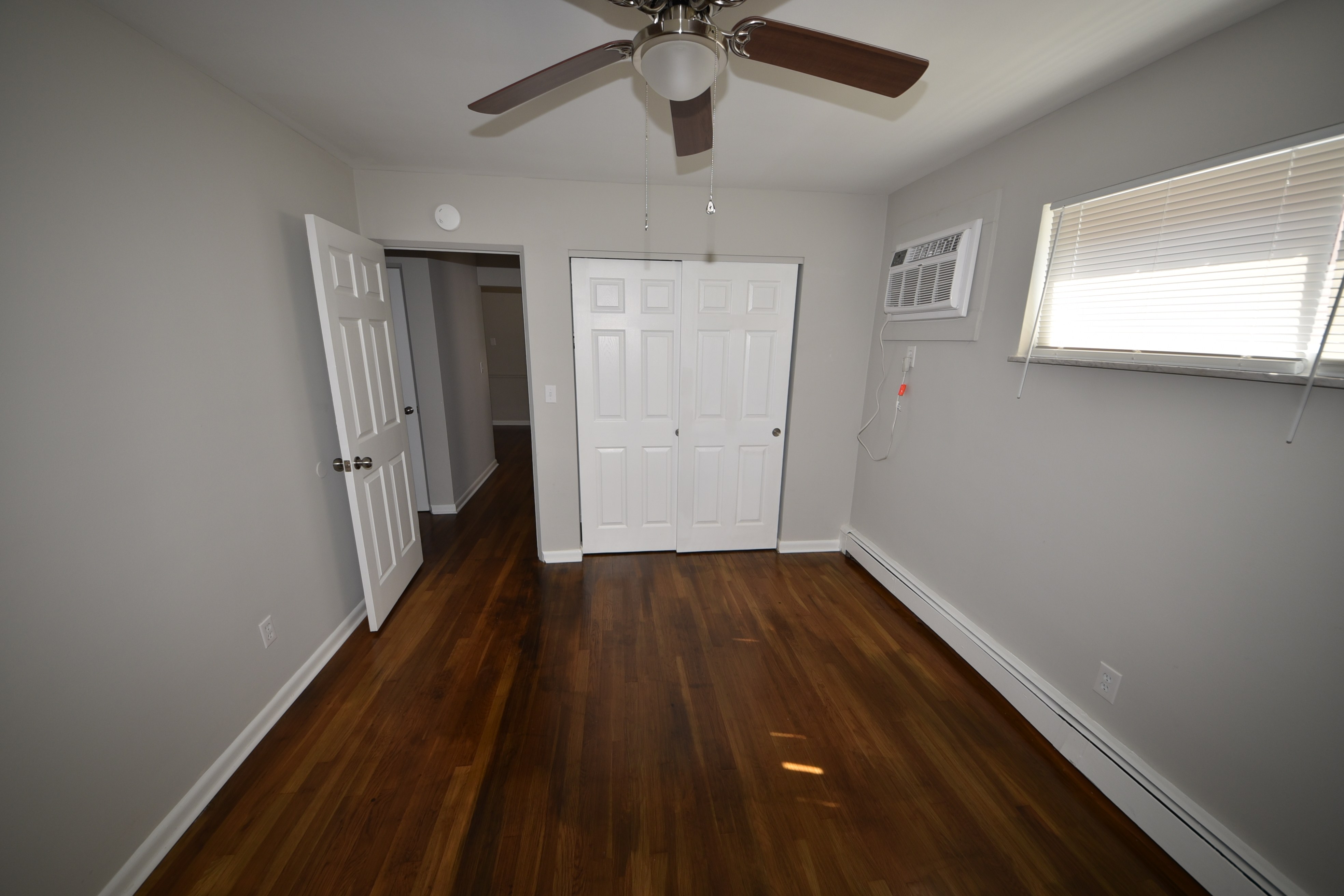 Bedroom with hardwood floors, closet, ceiling fan, and wall air conditioner